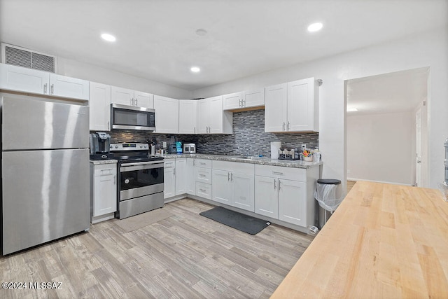 kitchen featuring light stone countertops, appliances with stainless steel finishes, light wood-type flooring, backsplash, and white cabinetry