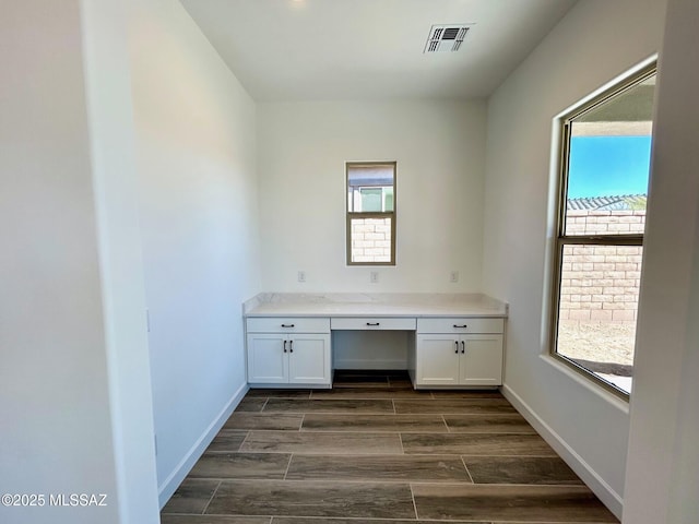 unfurnished office with wood finish floors, a healthy amount of sunlight, built in study area, and visible vents