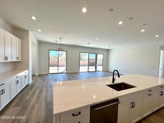 kitchen featuring white cabinetry, a sink, dishwashing machine, and light stone countertops