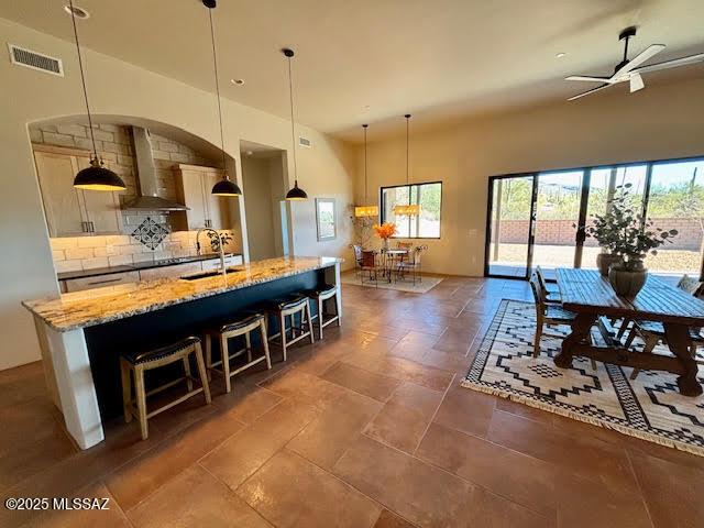 kitchen with sink, decorative light fixtures, light stone countertops, and wall chimney exhaust hood