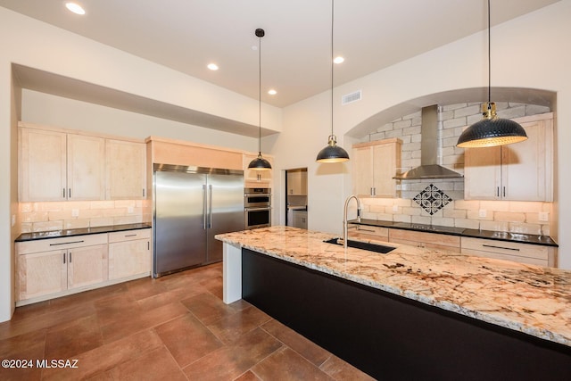 kitchen with sink, appliances with stainless steel finishes, decorative light fixtures, dark stone counters, and wall chimney exhaust hood