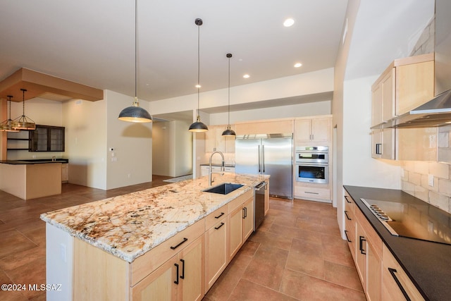 kitchen with wall chimney range hood, appliances with stainless steel finishes, hanging light fixtures, tasteful backsplash, and a center island with sink