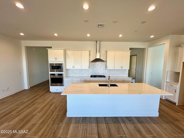 kitchen with wall chimney exhaust hood, appliances with stainless steel finishes, a sink, and white cabinetry