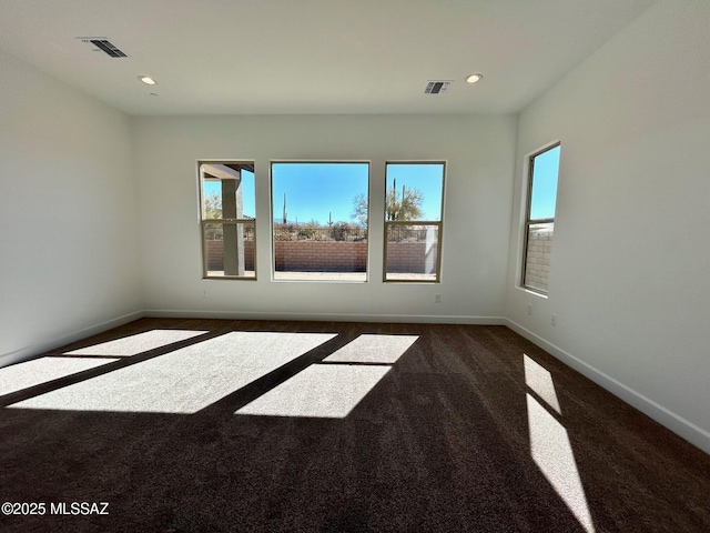 unfurnished room featuring dark colored carpet, visible vents, and a healthy amount of sunlight