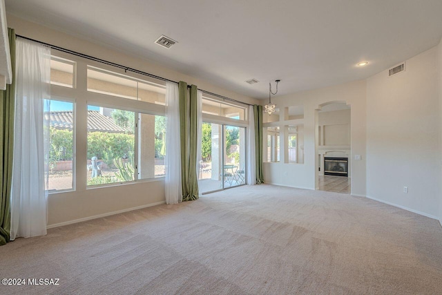 unfurnished living room featuring light colored carpet, built in features, and an inviting chandelier