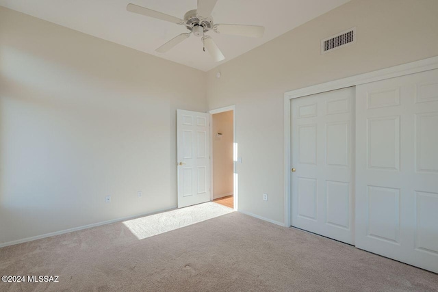 unfurnished bedroom featuring light carpet, a high ceiling, a closet, and ceiling fan