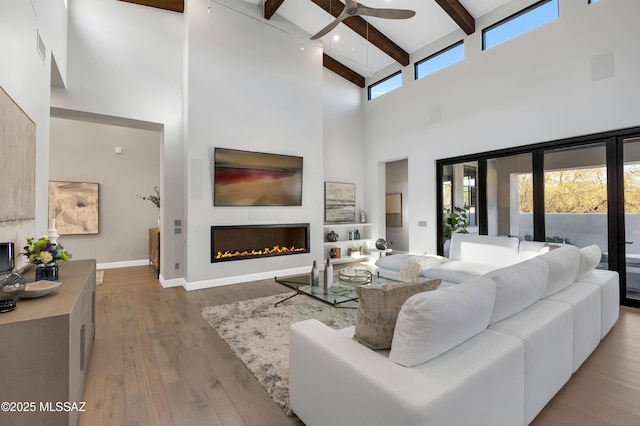 living room with ceiling fan, light hardwood / wood-style flooring, a high ceiling, and beamed ceiling