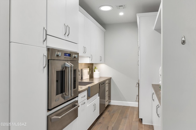 kitchen with hardwood / wood-style flooring, backsplash, white cabinets, and appliances with stainless steel finishes