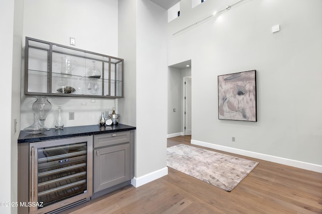 bar featuring beverage cooler, a high ceiling, gray cabinets, and light hardwood / wood-style flooring