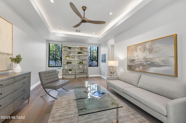 living room featuring hardwood / wood-style flooring, a tray ceiling, and ceiling fan