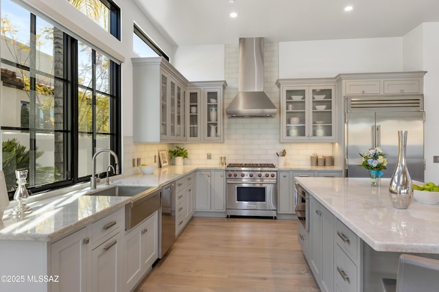 kitchen with decorative backsplash, built in appliances, light stone countertops, gray cabinetry, and wall chimney exhaust hood