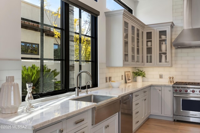 kitchen featuring wall chimney exhaust hood, black dishwasher, sink, premium range, and light stone counters