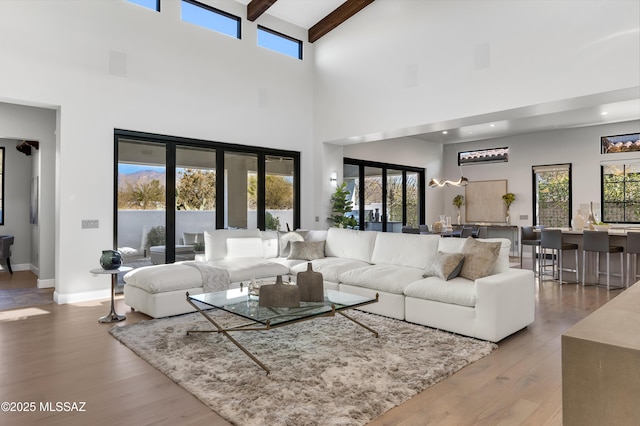 living room featuring a high ceiling, light hardwood / wood-style flooring, beam ceiling, and french doors