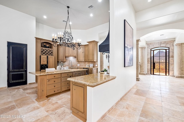 kitchen featuring an island with sink, arched walkways, visible vents, a chandelier, and stone tile flooring