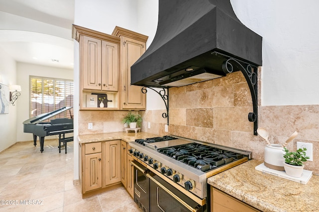 kitchen with range hood, arched walkways, range with two ovens, light brown cabinets, and backsplash