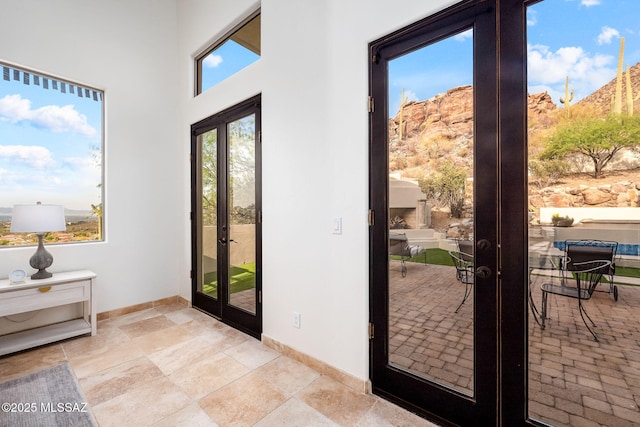 doorway with a high ceiling, french doors, baseboards, and stone tile floors