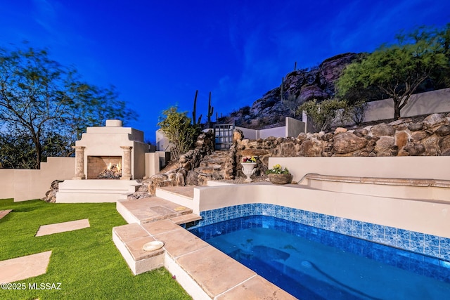 view of pool featuring a lit fireplace, a jacuzzi, fence, and a lawn