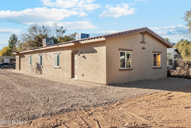 back of property with a tile roof, central AC, and stucco siding