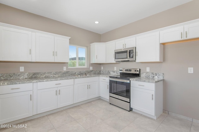 kitchen with baseboards, light stone countertops, stainless steel appliances, white cabinetry, and a sink