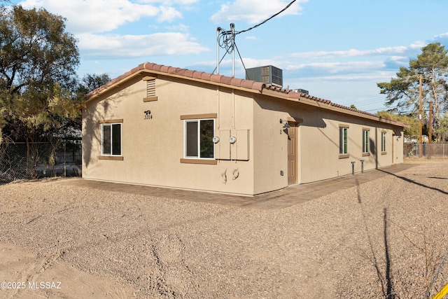 rear view of house featuring central AC unit, fence, and stucco siding