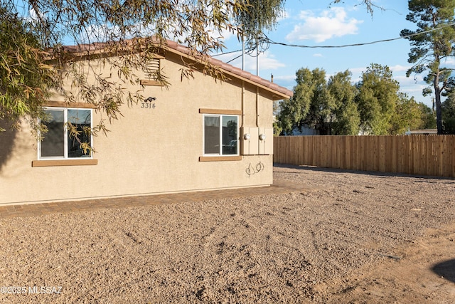 view of property exterior with a tile roof, fence, and stucco siding