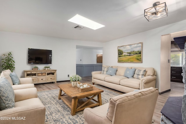 living room with a skylight, light hardwood / wood-style flooring, and an inviting chandelier