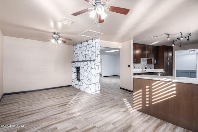 unfurnished living room with ceiling fan, a fireplace, sink, and light wood-type flooring