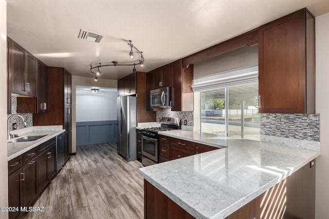 kitchen featuring backsplash, sink, light wood-type flooring, appliances with stainless steel finishes, and kitchen peninsula