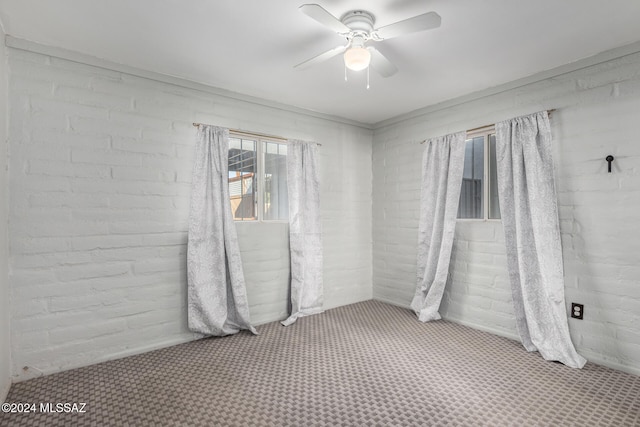 carpeted empty room with ceiling fan and brick wall