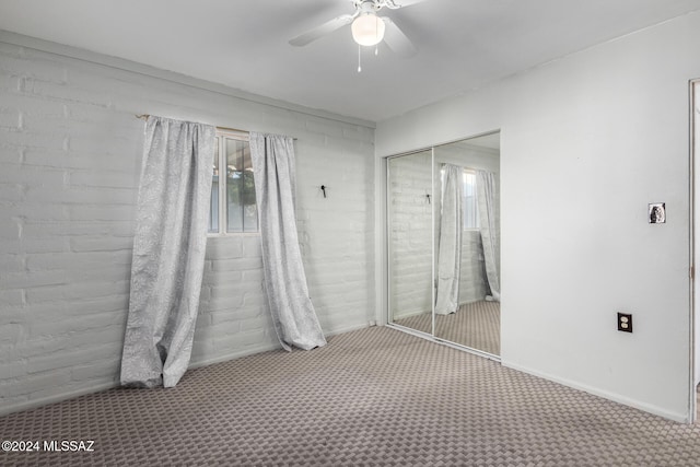 unfurnished bedroom with carpet flooring, ceiling fan, brick wall, and a closet