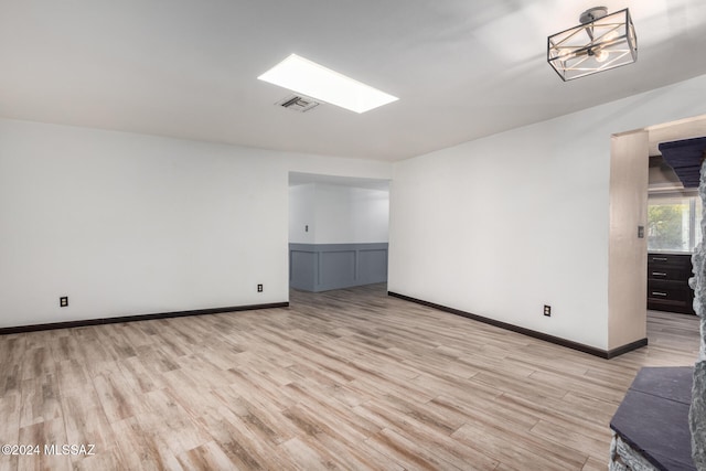 unfurnished room featuring a skylight and light hardwood / wood-style floors