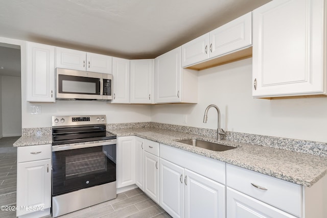 kitchen featuring light stone countertops, wood tiled floor, stainless steel appliances, white cabinetry, and a sink