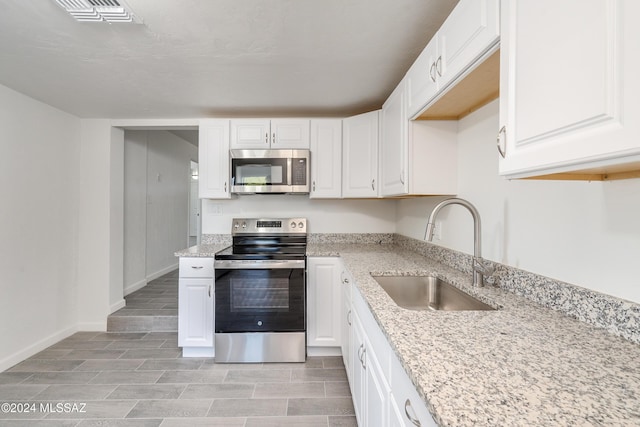 kitchen featuring visible vents, white cabinets, light stone countertops, stainless steel appliances, and a sink