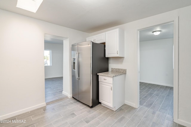 kitchen with a skylight, stainless steel fridge, baseboards, light countertops, and white cabinetry