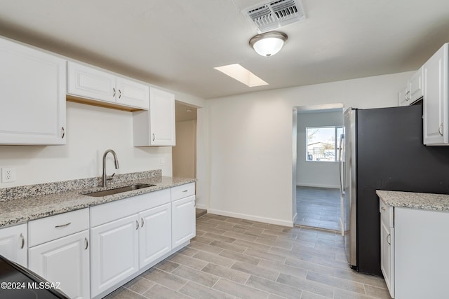 kitchen with a skylight, a sink, visible vents, white cabinetry, and freestanding refrigerator