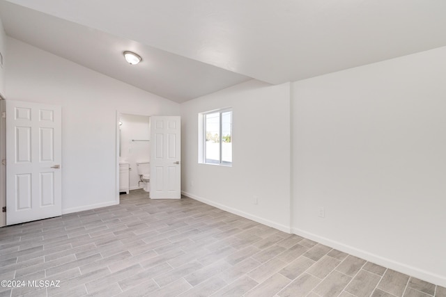 unfurnished bedroom featuring light wood-style flooring, baseboards, ensuite bath, and vaulted ceiling