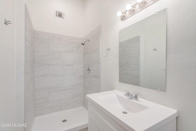 bathroom with visible vents, a tile shower, and vanity