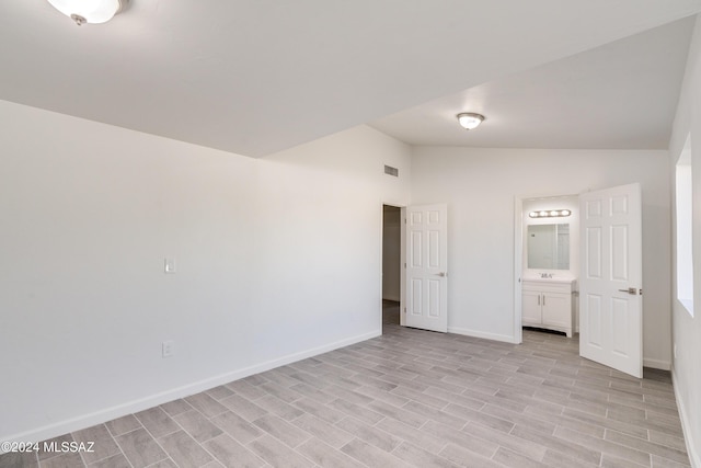 unfurnished bedroom with ensuite bathroom, light wood-style flooring, visible vents, baseboards, and vaulted ceiling