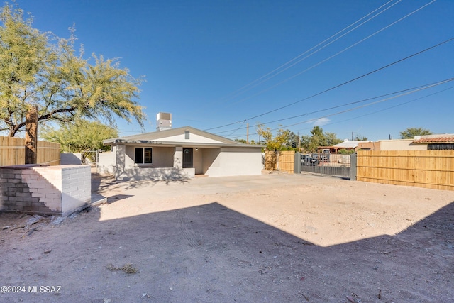 rear view of property featuring a chimney, stucco siding, fence, and a gate