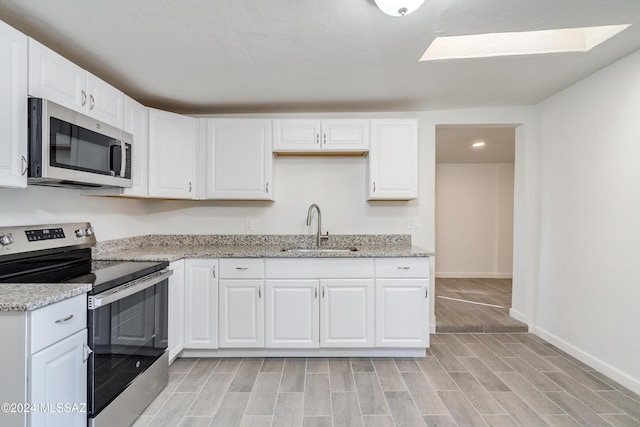 kitchen featuring stainless steel appliances, a sink, light stone countertops, and white cabinets