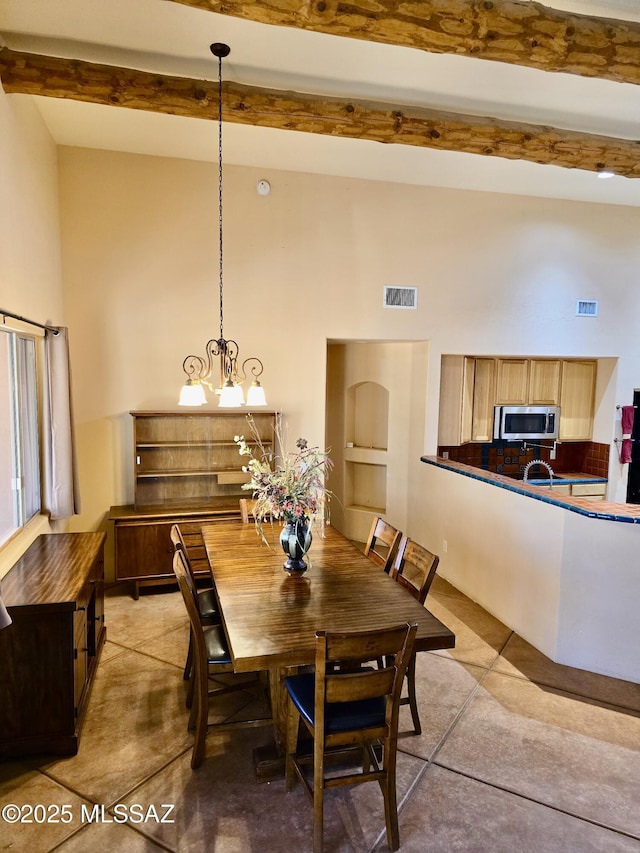 dining space featuring a towering ceiling, built in shelves, beam ceiling, and a chandelier