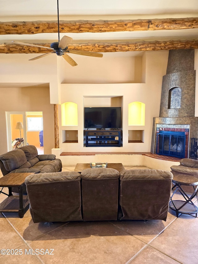 living room with ceiling fan, built in features, a tile fireplace, and beamed ceiling
