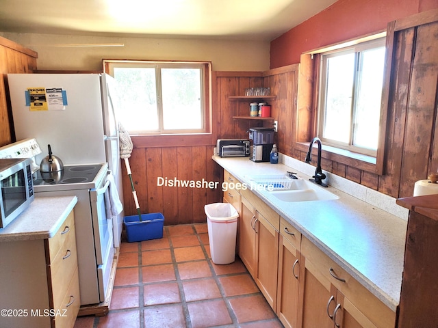 kitchen featuring a healthy amount of sunlight, sink, wooden walls, and white appliances