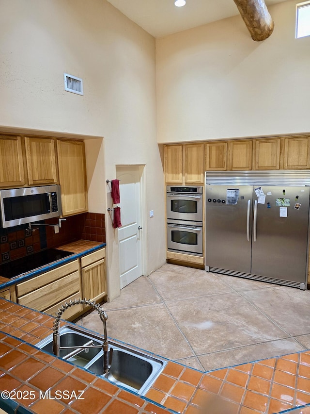kitchen featuring stainless steel appliances, a high ceiling, tile counters, and sink