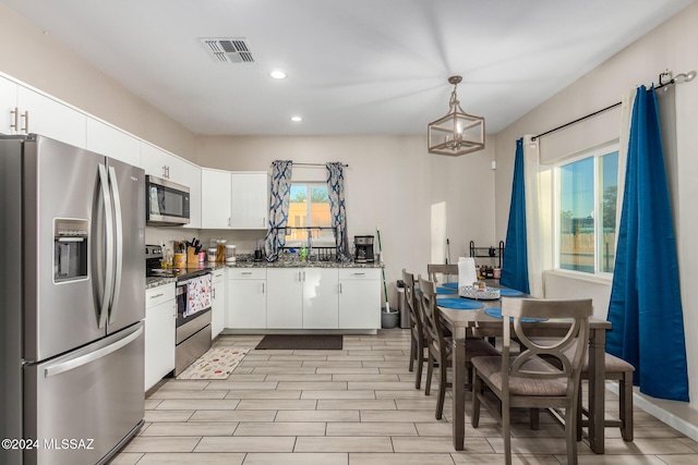 kitchen with a wealth of natural light, pendant lighting, white cabinets, and stainless steel appliances