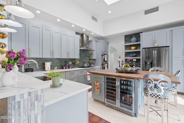 kitchen featuring stainless steel appliances, light stone counters, wall chimney exhaust hood, backsplash, and decorative light fixtures