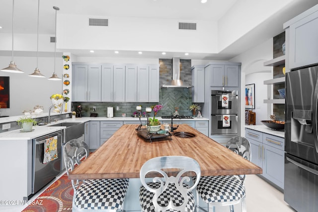 kitchen with stainless steel appliances, wall chimney exhaust hood, gray cabinetry, pendant lighting, and decorative backsplash