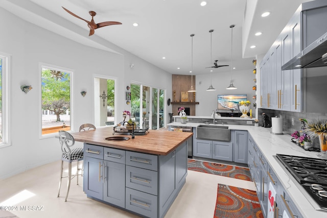 kitchen with tasteful backsplash, wall chimney range hood, gas cooktop, hanging light fixtures, and sink