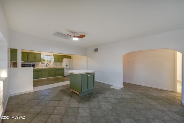 kitchen with ceiling fan, sink, white refrigerator with ice dispenser, a kitchen island, and green cabinetry