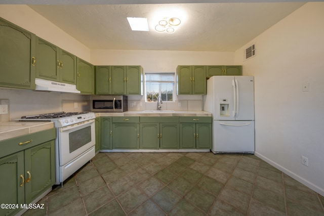 kitchen with white appliances, dark tile patterned floors, green cabinets, and sink